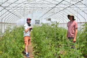 Chris Darche and Zach Cannady are standing in a greenhouse and smiling toward the camera.